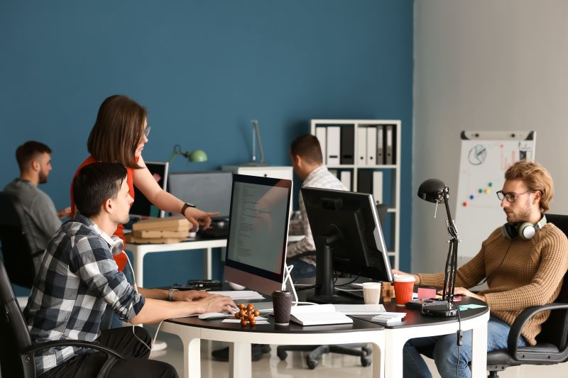 Equipe usando computadores e conversando em um escritório a respeito da otimização de processos da empresa.