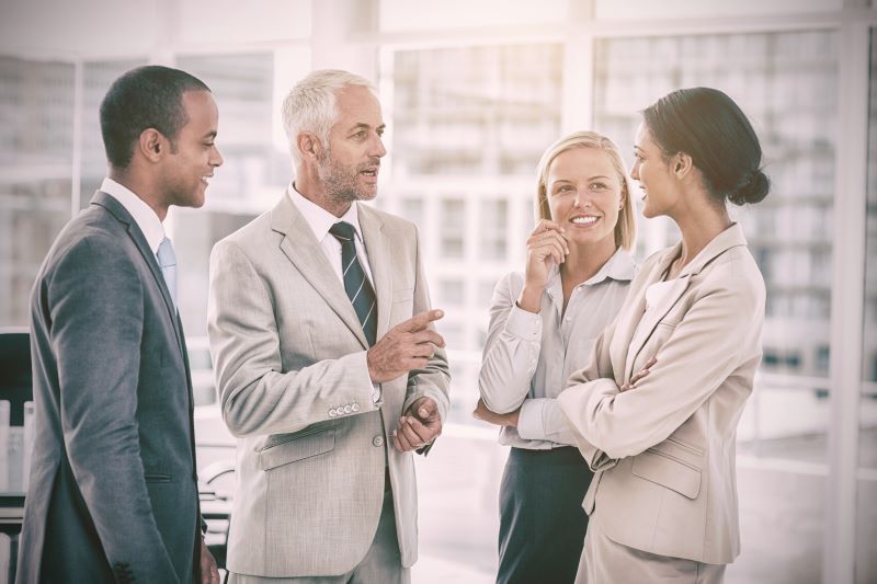 Grupo de profissionais composto por duas mulheres e dois homens conversa em um ambiente de negócios.