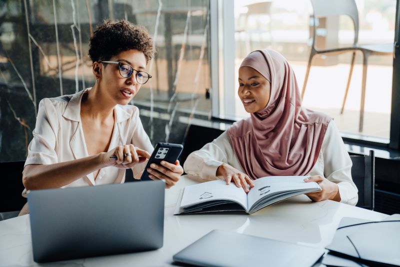 Relações humanas no trabalho: duas mulheres de culturas diferentes conversando e interagindo no escritório.