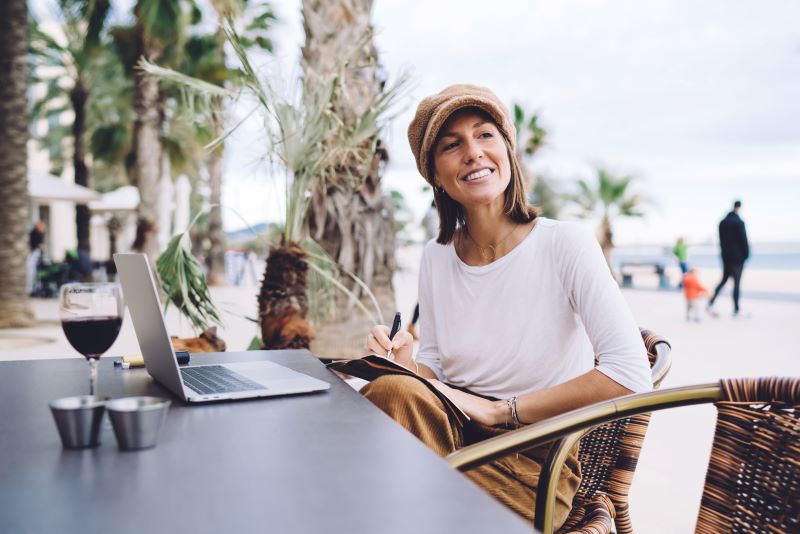 Modelo híbrido: mulher trabalhando em área externa, usando notebook, caneta e caderno.