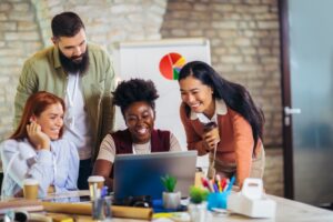 Tipos de cultura organizacional: equipe sorridente reunida em volta de computador.